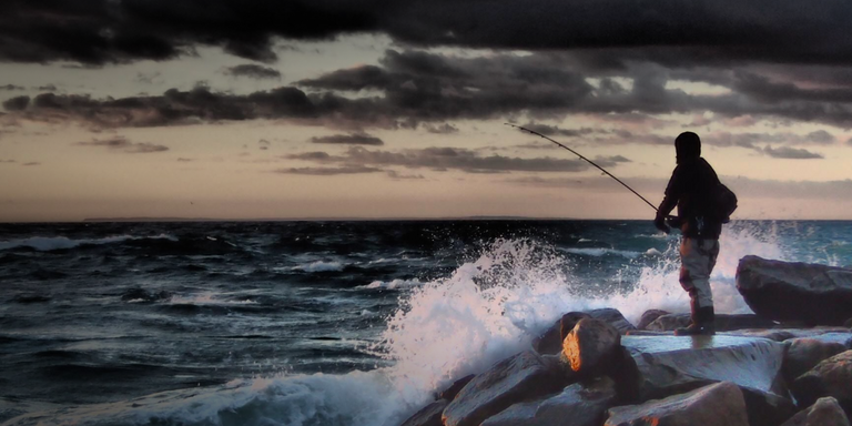 Guy standing on rock fishing with large waves